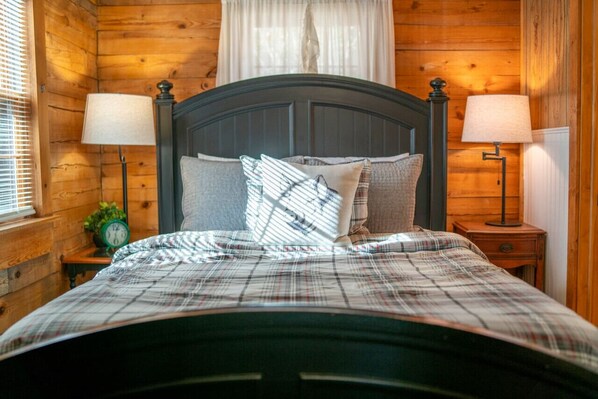 Un dormitorio de estilo cabaña de madera con cama, dos lámparas de noche y un reloj sobre una mesita.