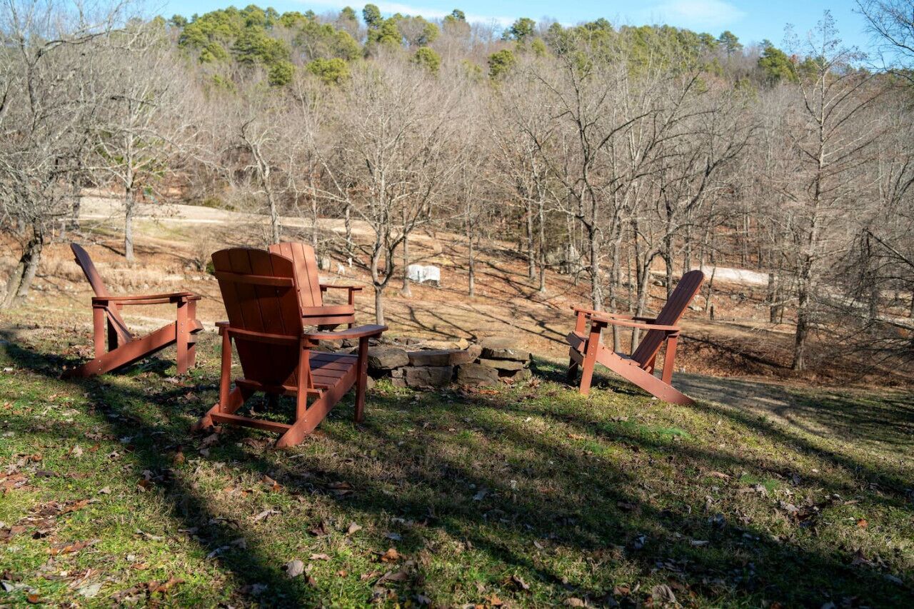 Een rustieke buitenruimte met houten stoelen en banken, omgeven door bomen en een stenen muur.