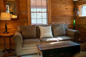 Una habitación acogedora con una pared de madera, un sofá con un cojín, una lámpara y una ventana con persianas.
