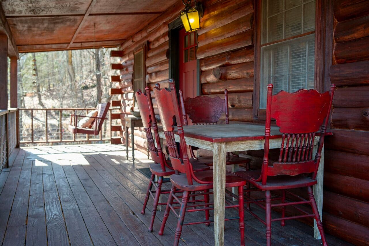 Une terrasse en bois avec une table et des chaises, une échelle et une fenêtre avec des volets.