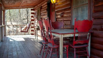 Une terrasse en bois avec une table et des chaises, une échelle et une fenêtre avec des volets.