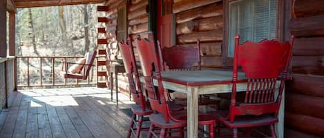A wooden deck with a table and chairs, a ladder, and a window with shutters.