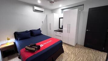 A bedroom with a bed, a wardrobe, a desk, and an air conditioning unit.
