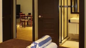 A hotel room with a bed, a bathroom with a mirror, and a dining area visible through an open door.