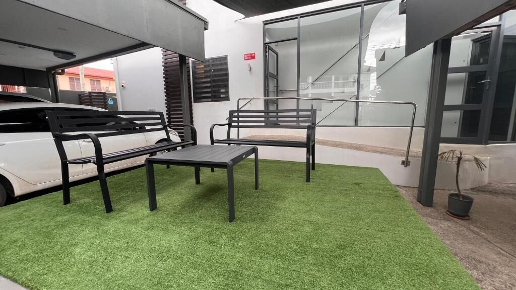 Un espacio de descanso al aire libre con césped artificial, dos bancos de metal negro y una mesa.