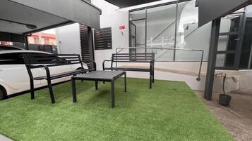 Un espacio de descanso al aire libre con césped artificial, dos bancos de metal negro y una mesa.