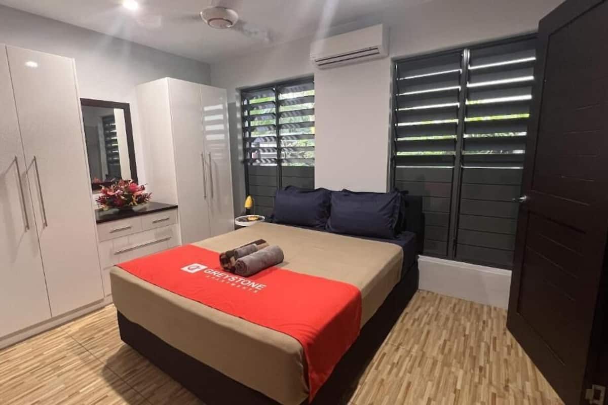 A bedroom with a bed, a wardrobe, a mirror, and a window with blinds.