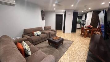 A modern living room with a brown sectional sofa, a small ottoman, and a dining area with a wooden table and chairs.