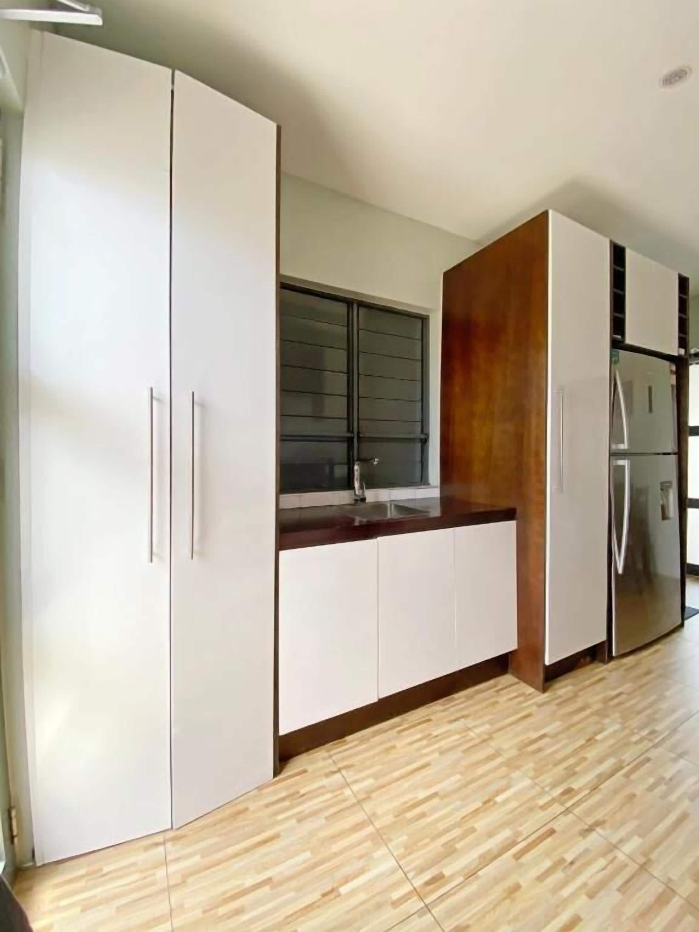 A modern kitchen with white cabinets, a wooden countertop, and a stainless steel refrigerator.