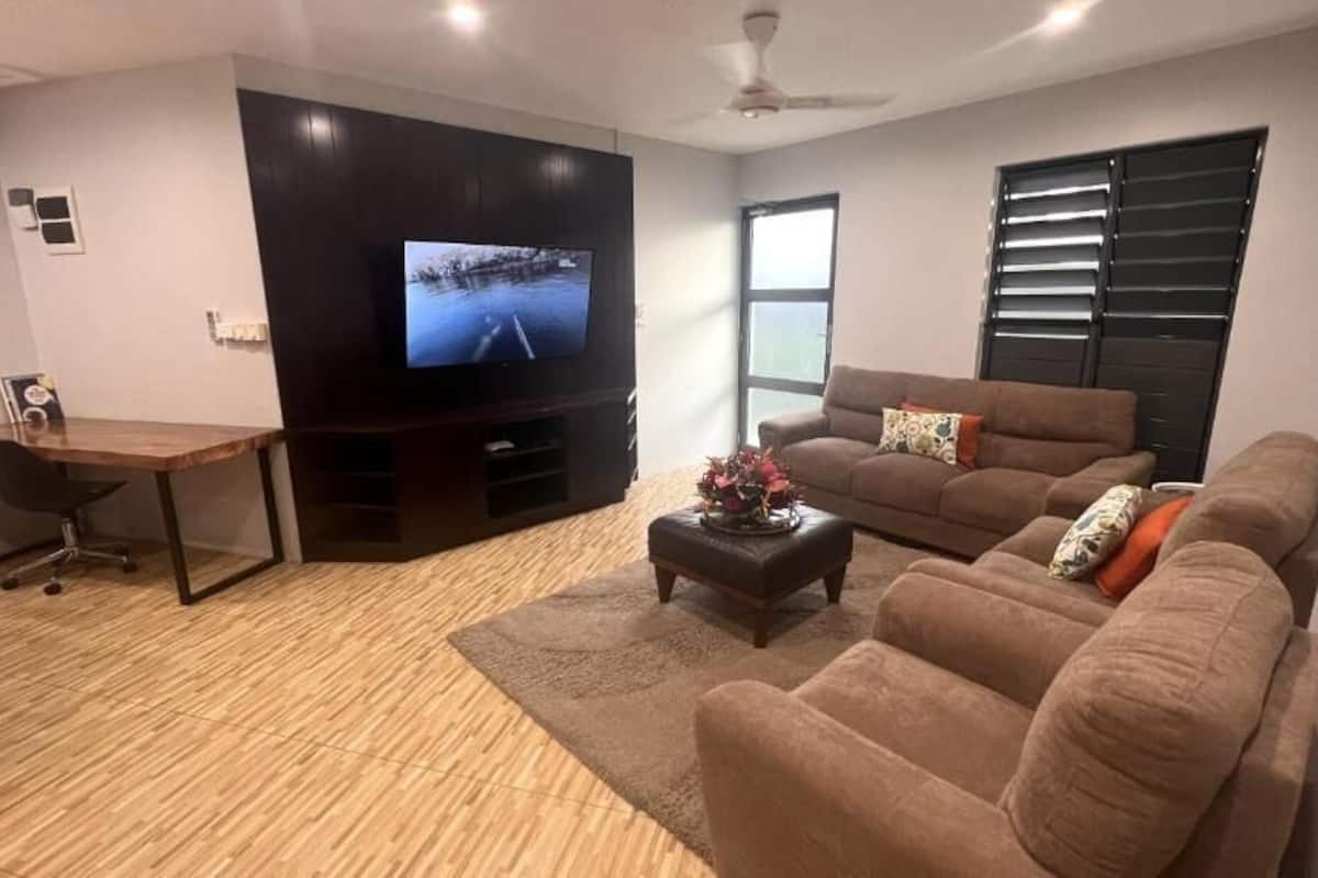 A living room with a flat-screen TV, a brown sofa, a coffee table, and a wooden desk.
