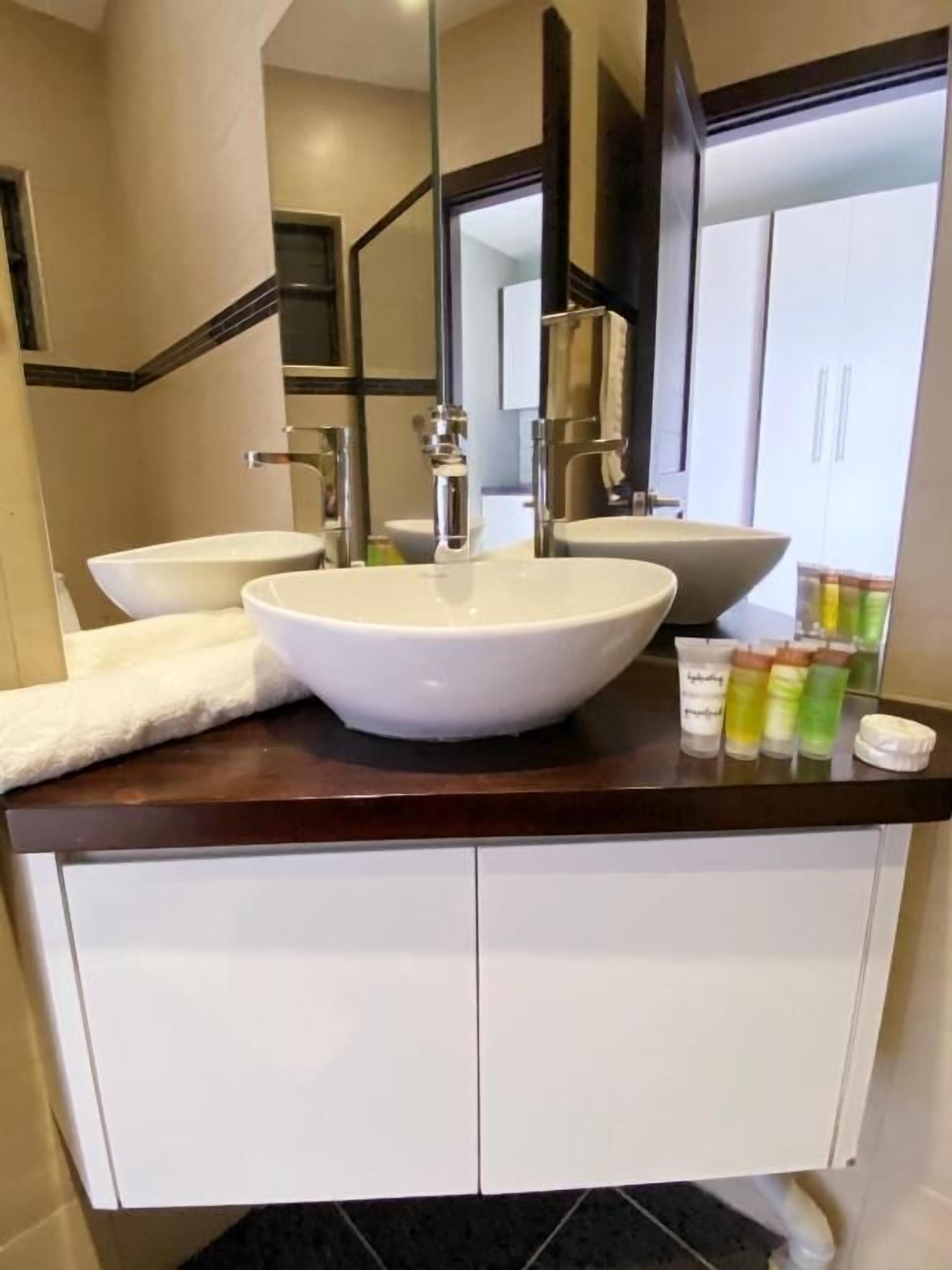 Un bagno moderno con un lavandino grande al centro, due lavandini più piccoli sui lati e uno specchio sopra il lavandino centrale. Ci sono articoli da toilette sul piano di lavoro.