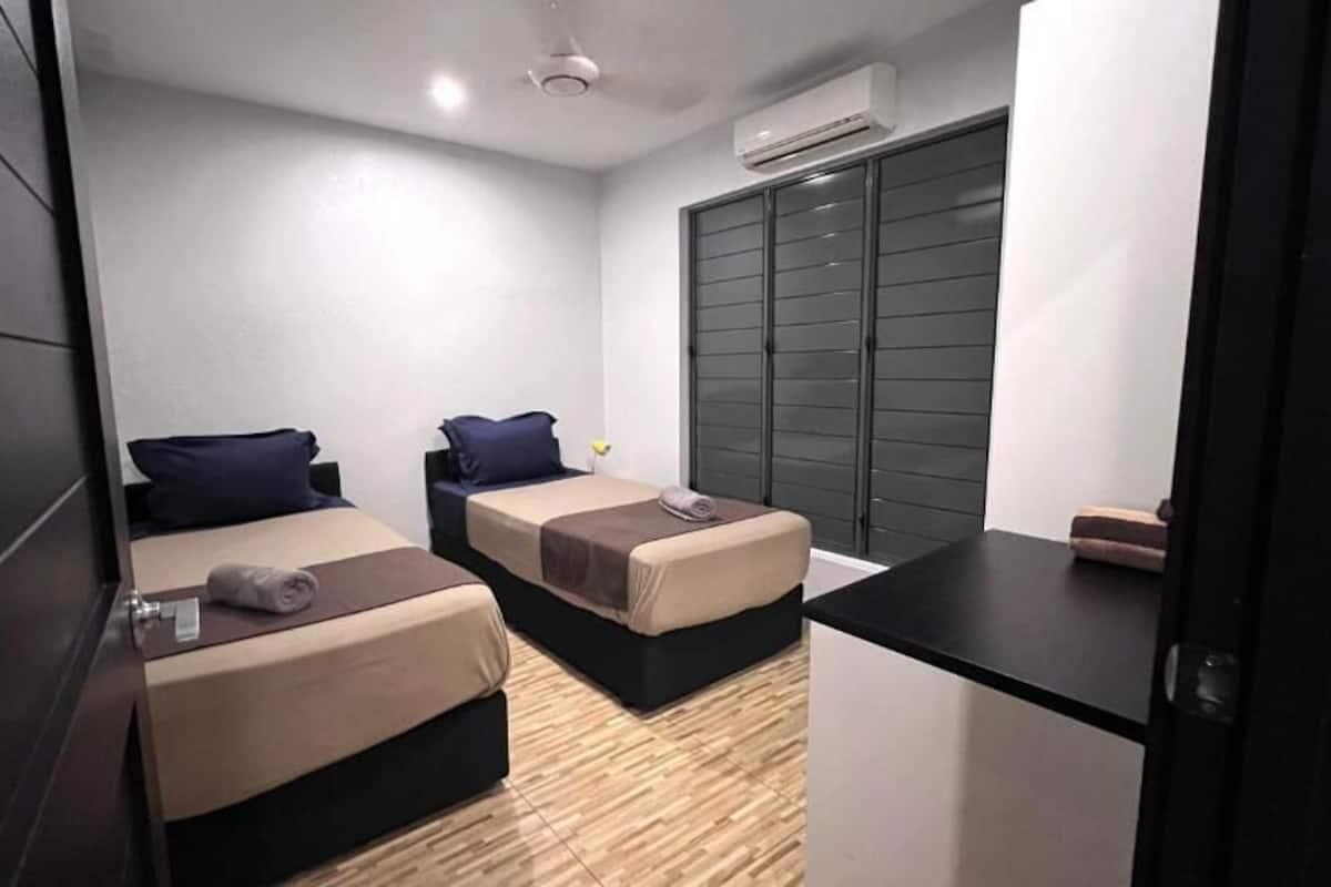A compact hotel room with two single beds, a small desk, a wardrobe, and an air conditioning unit.