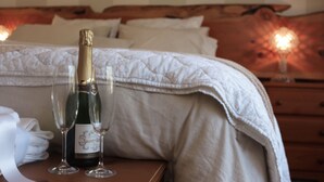 Un lit avec une tête de lit en bois, une bouteille de champagne et deux verres posés sur une table de chevet.