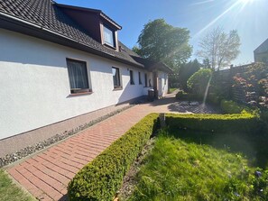 A building with a white exterior, a tiled roof, and a paved walkway leading to a hedge.