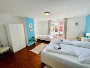 Et hotelværelse med seng, skab, vindue med gardiner, radiator og et lille bord med lampe.