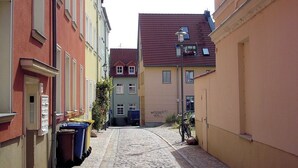 A cobblestone street flanked by buildings with a mix of architectural styles, including a red building with a white window frame and a yellow building with a red roof. - Apartment Bernstein - Ferienwohnung Bernstein Ruhig mit Garten (Rostock)