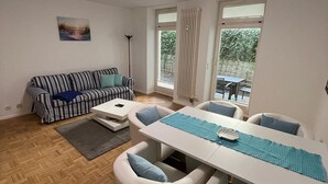 A modern living room with a sofa, a dining table with chairs, and a floor lamp. - Apartment Bernstein - Ferienwohnung Bernstein Ruhig mit Garten (Rostock)
