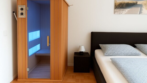 A bedroom with a bed, a nightstand, a wooden wardrobe with a blue interior, and a painting on the wall. - Apartment Bernstein - Ferienwohnung Bernstein Ruhig mit Garten (Rostock)