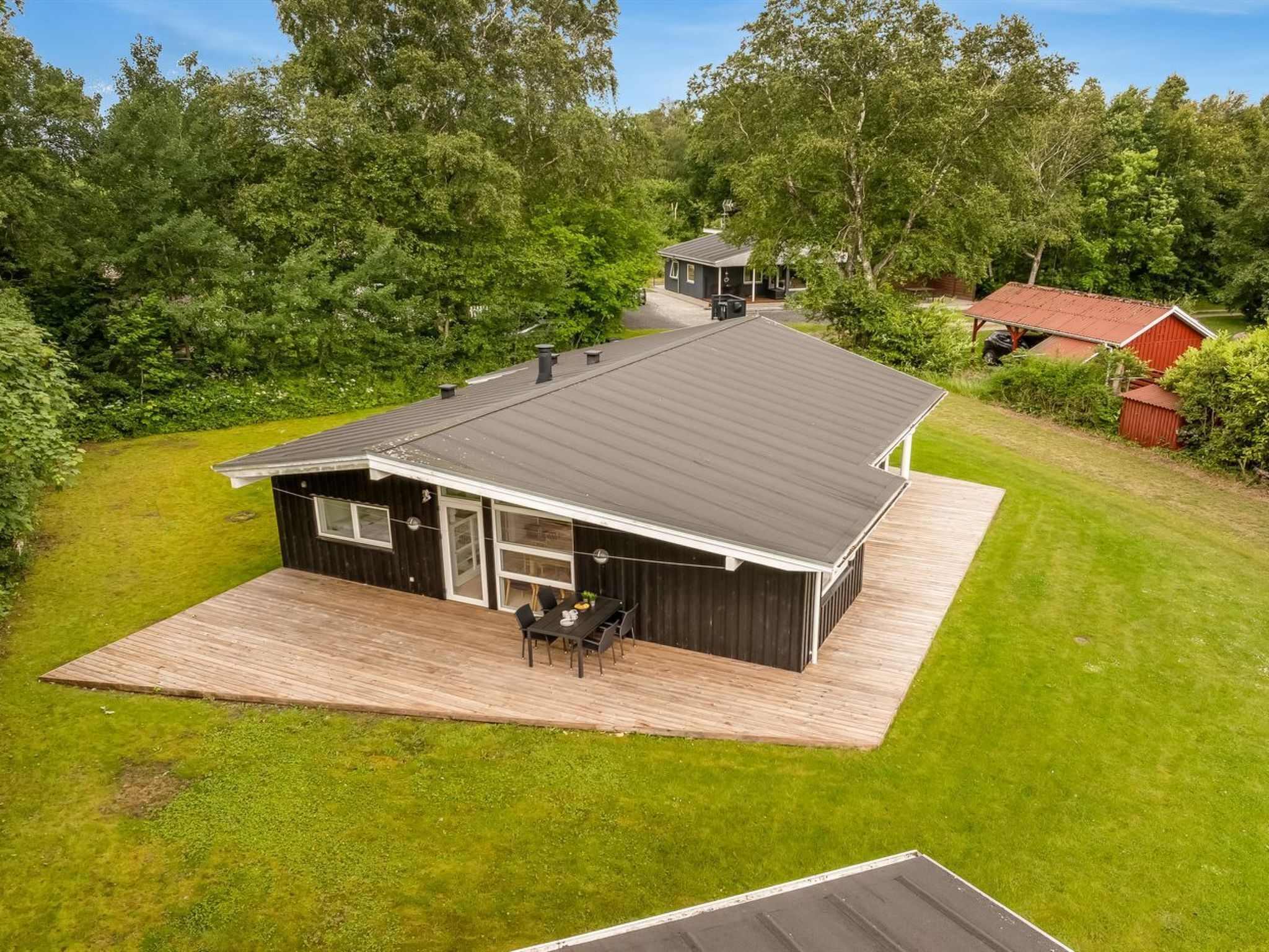 Een modern huis met een groot terras, een garage en een rode schuur op de achtergrond.