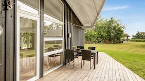 A modern outdoor patio with a wooden deck, a glass sliding door, and a dining table with chairs. - "Majvor" - 200m from the sea by Interhome (Hadsund)