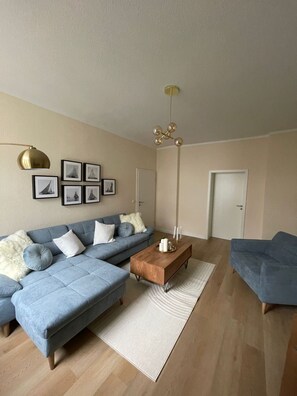 A modern living room with a blue sectional sofa, a wooden coffee table, and a floor lamp.