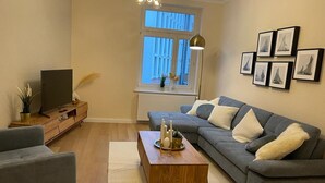 A modern living room with a grey sofa, a wooden coffee table, and a television on a wooden stand.