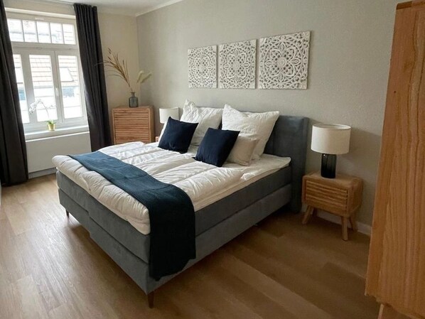 A bedroom with a bed, bedside tables, a window with curtains, and wall art.
