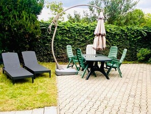 Une terrasse avec une table et des chaises, un parasol et des fauteuils de jardin.