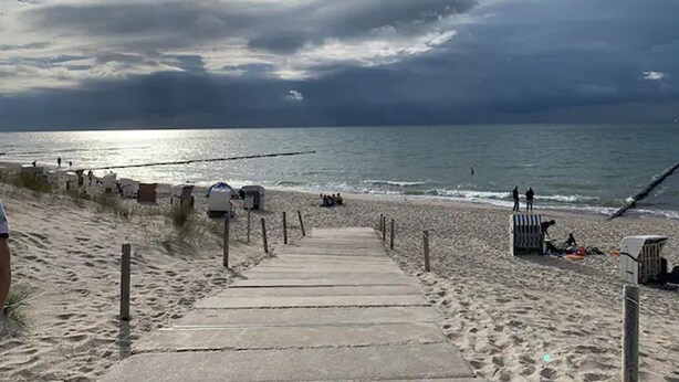 Un sendero de concreto que lleva a la playa, con vista al océano y un cielo nublado.