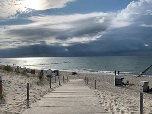 Un chemin en béton menant à la plage, avec vue sur l’océan et un ciel nuageux.
