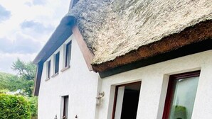 Un edificio blanco con techo de paja, un patio empedrado y una banca.