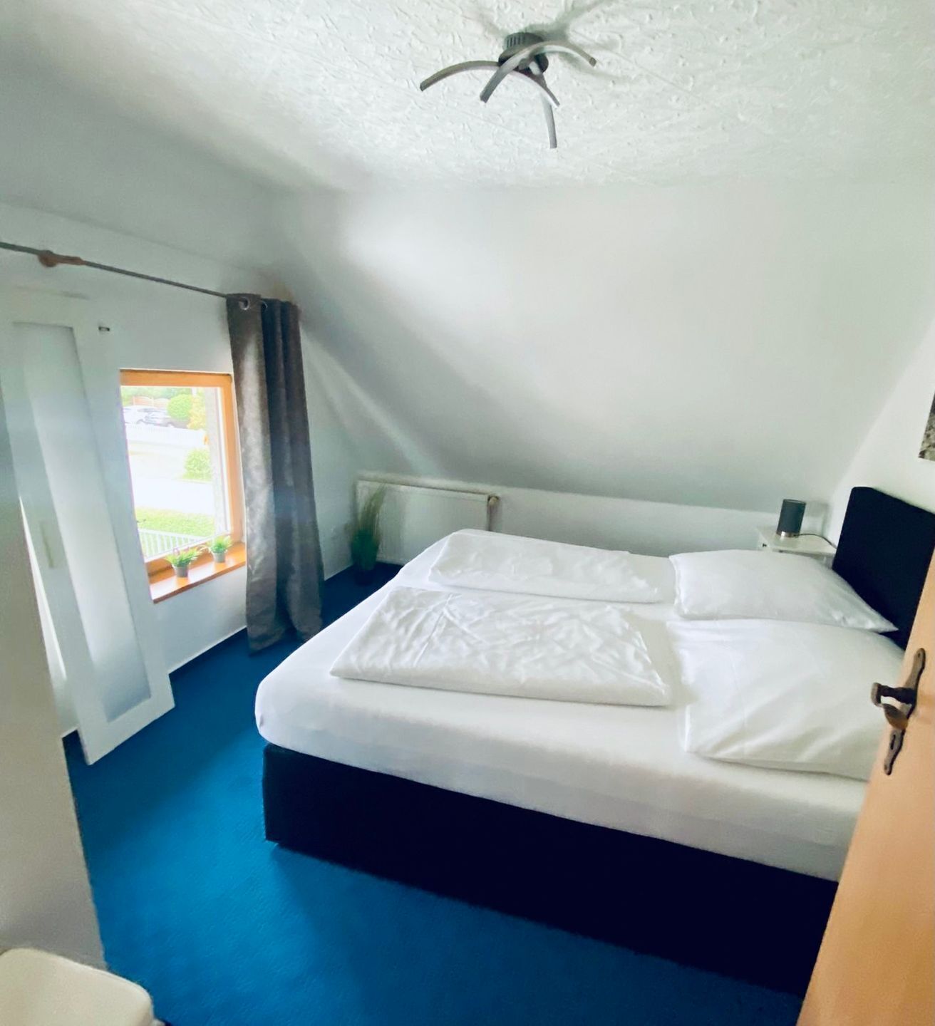Ein Schlafzimmer mit Bett, einem Vorhangfenster, einem Deckenventilator und Blick ins Freie.