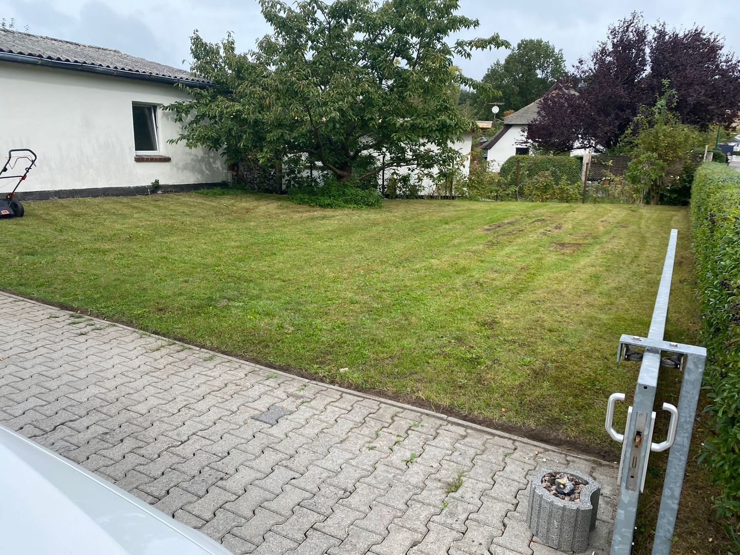 Une cour résidentielle avec une allée pavée, une tondeuse à gazon et un portail en métal.