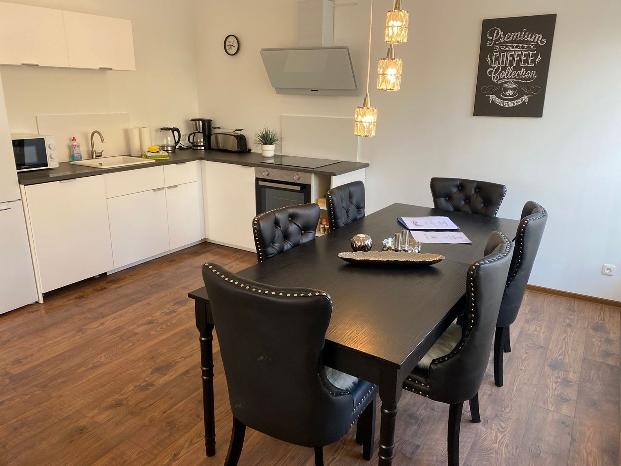 A modern kitchen with white cabinets, a dining table with black chairs, and a coffee collection sign on the wall.