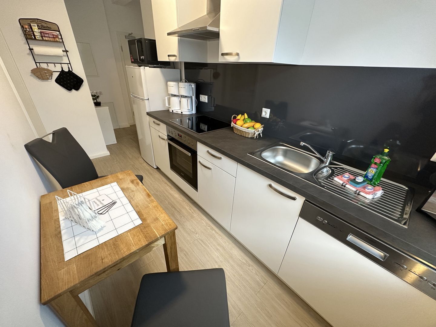 Een kleine keuken met een magnetron, koffiezetapparaat en een mand met fruit op het aanrecht.