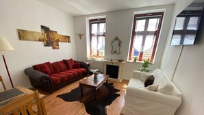 Una sala de estar con un sofá rojo, un sofá blanco, una mesa de centro de madera, una chimenea y un televisor montado en la pared.