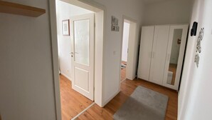 Un pasillo con paredes blancas y suelo de madera, que conduce a una habitación con un armario y una puerta de vidrio esmerilado.