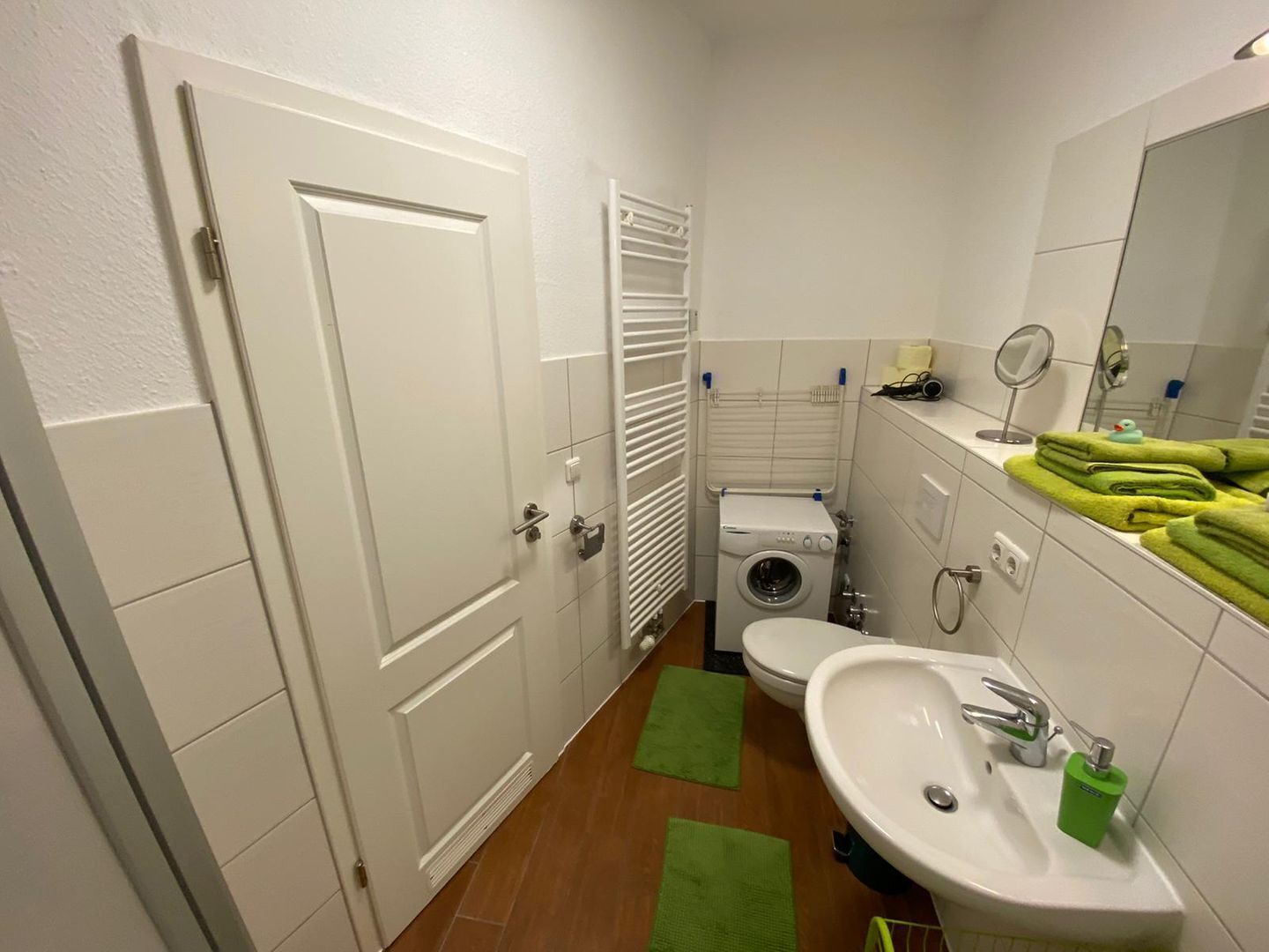 Un baño pequeño con lavadora, inodoro, lavamanos y un perchero para toallas.