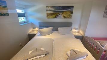 Ein Doppelbett mit zwei Kissen, ein Nachttisch mit Lampe, ein Bild an der Wand und ein Fenster mit Jalousien.