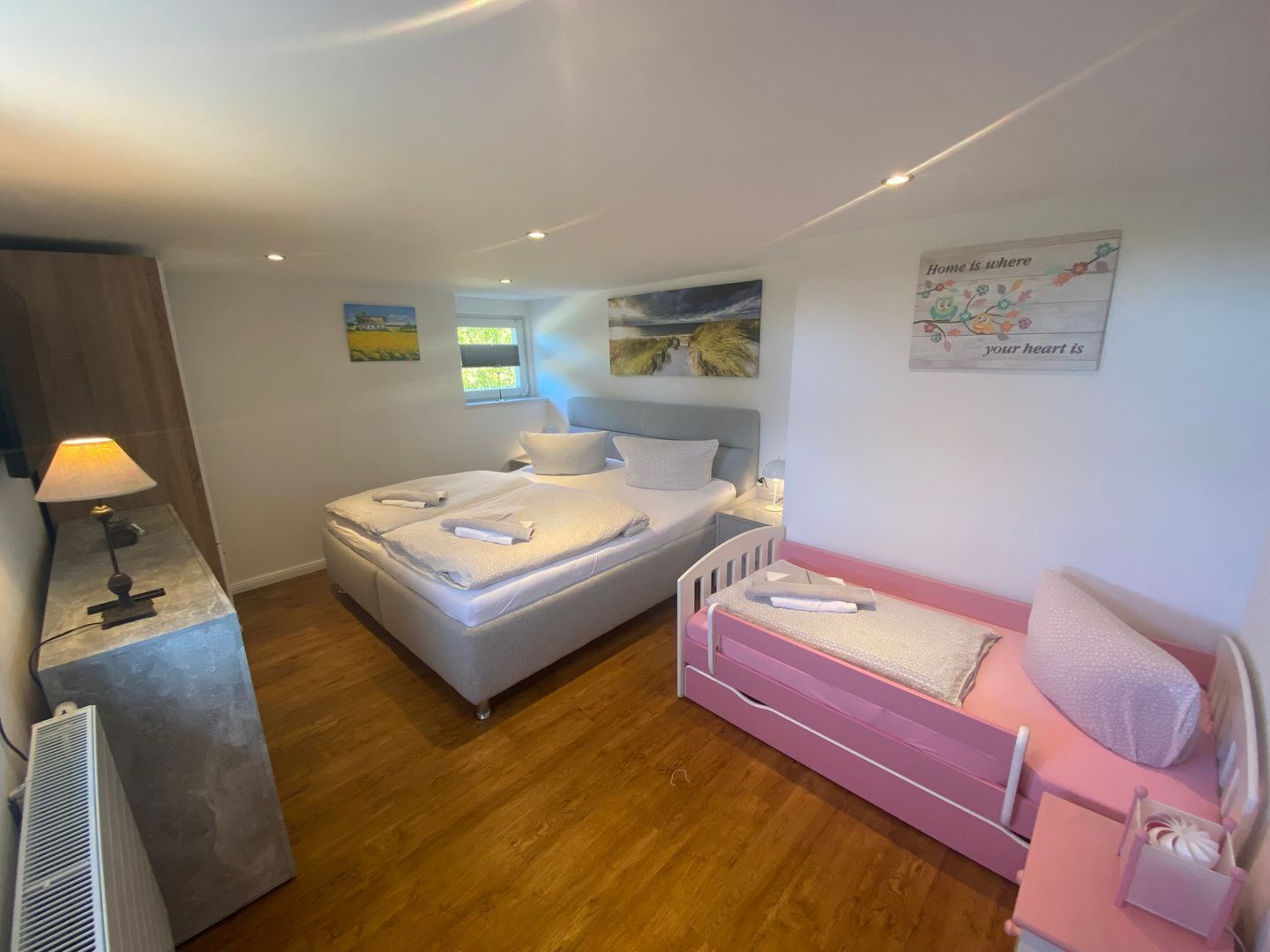 Un dormitorio con cama, mesita de noche, lámpara, calentador, ventana y una pared con un póster.