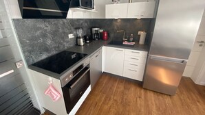 Ett modernt kök med en svart spishäll, vita skåp, ett kylskåp i rostfritt stål och en mikrovågsugn placerad ovanför skåpen.