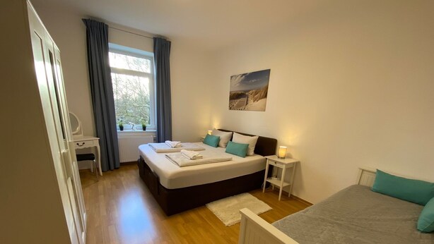 Une chambre à coucher avec un lit double, un lit simple, un bureau et une fenêtre avec des rideaux.