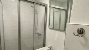 Une salle de bain avec une douche à parois de verre, un lavabo avec un miroir et un porte-serviettes.