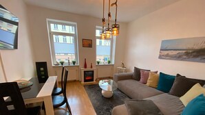 Un salon moderne avec un canapé, une table basse et un coin repas. On y trouve des fenêtres équipées de stores, une cheminée et un tableau accroché au mur.