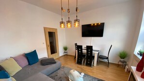 Un salon moderne avec un canapé gris, une table basse, un téléviseur à écran plat et un coin repas comprenant des chaises et une petite table.