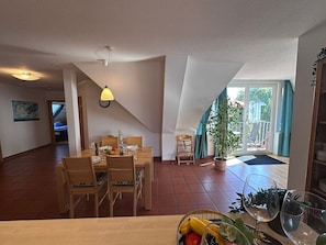 A dining area with a wooden table and chairs, a hanging light fixture, and a view of the outdoors through a glass door. - Ostseeanker Ferienhaus mit Großem Garten, kl. Eigener Fußballplatz, Smart-tv, Grill - Ostsee-anker (Zingst)