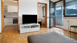Un salon moderne comprenant un téléviseur, un canapé, une table à manger et un coin cuisine visible à travers une porte ouverte.
