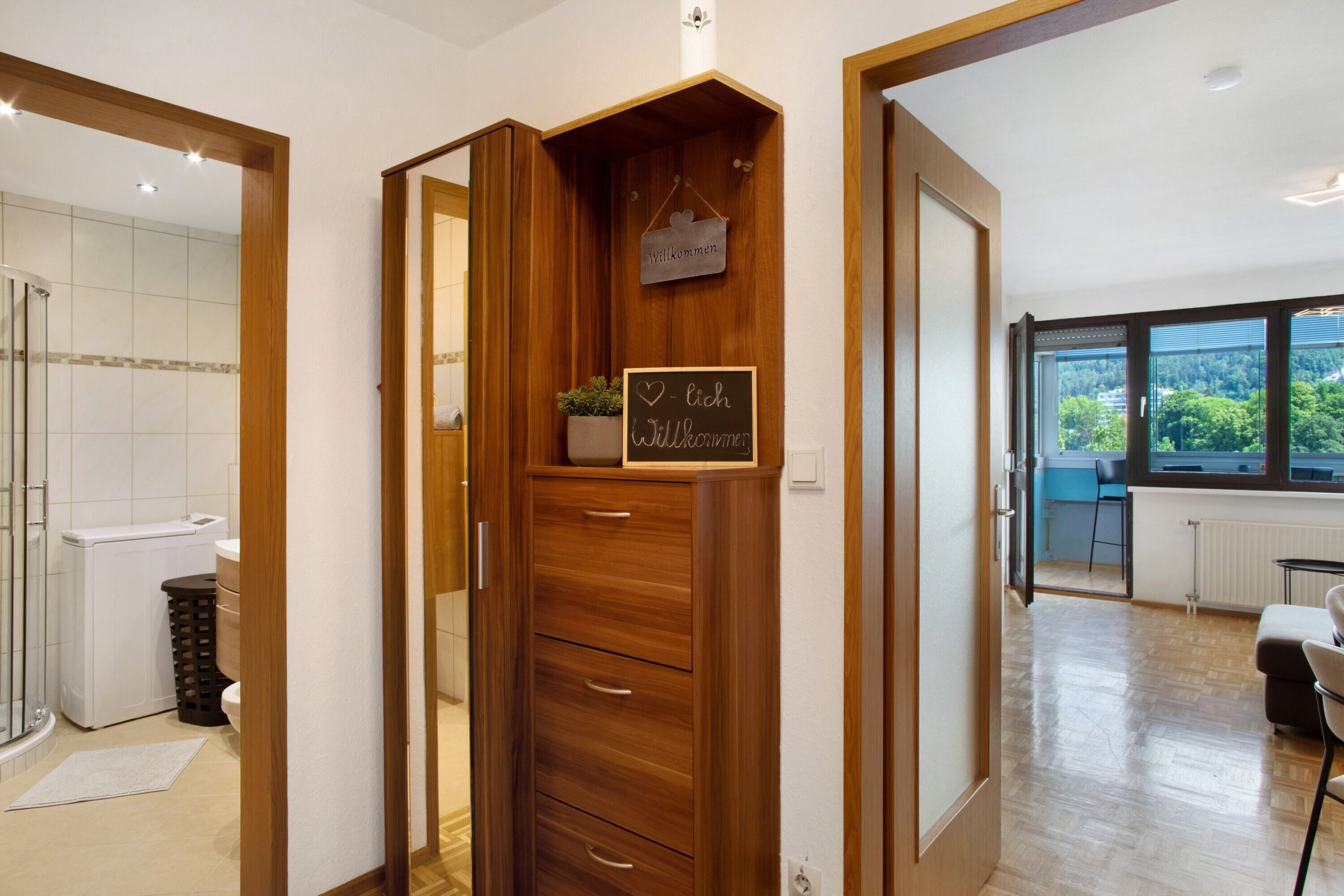 A modern bathroom with a shower, toilet, and a wooden cabinet with a welcome sign.