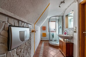 Ein Badezimmer mit Steinwand, Duschkabine aus Glas, Holzschrank und weißem Waschbecken.