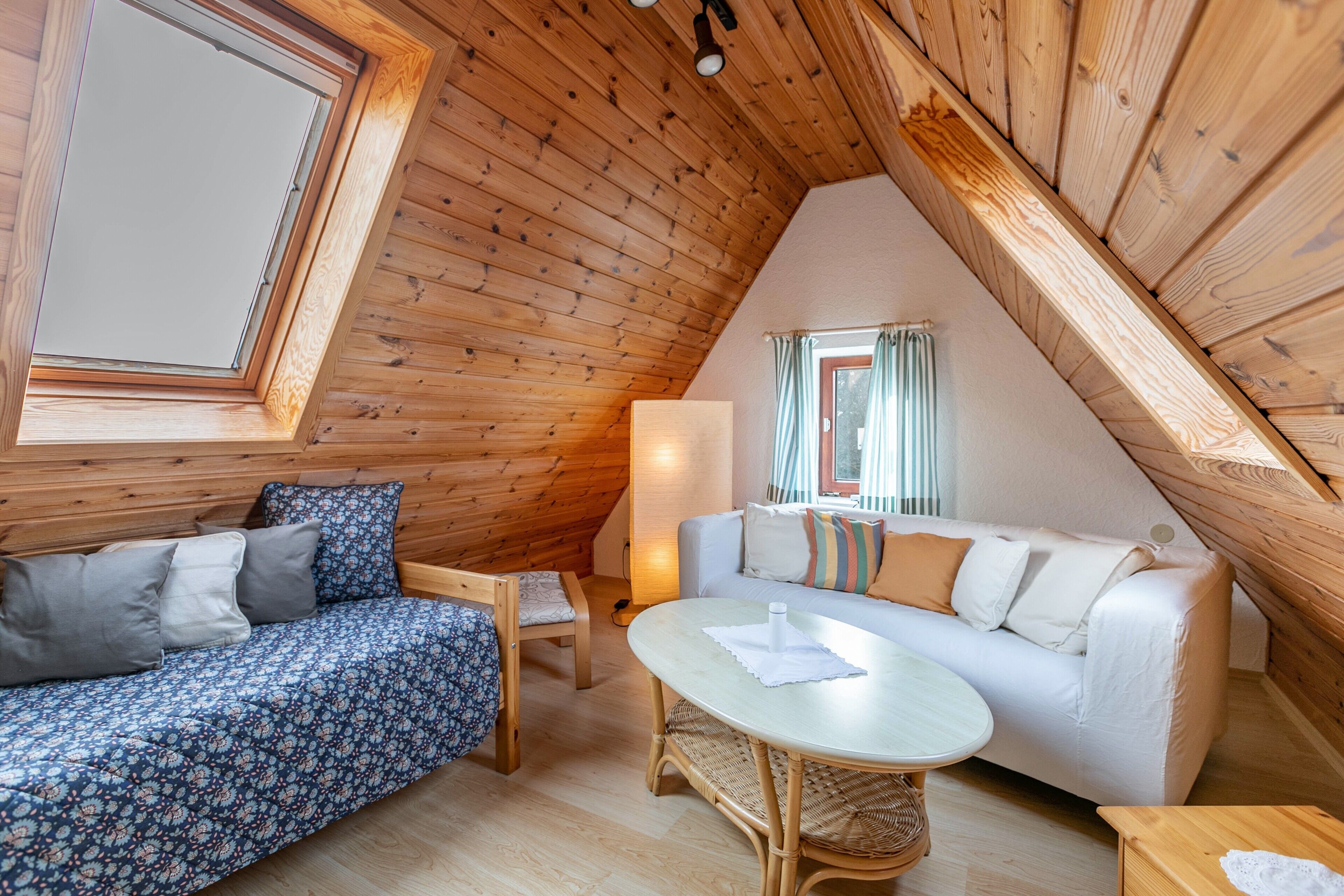 Une pièce chaleureuse avec un plafond en pente, un canapé, une petite table et une fenêtre avec des rideaux.